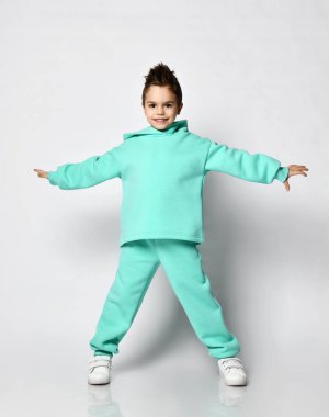 Gülümseyen, şık saç kesimi olan, modern yeşil, nane renginde spor giyimli kapüşonlu çocuk el ele tutuşup duruyor.