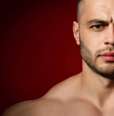 Acımasız, tıraşsız, vücudunun üst kısımlarında çıplak bir şekilde kameraya bakan genç ve güçlü bir adamın yakın plan portresi.