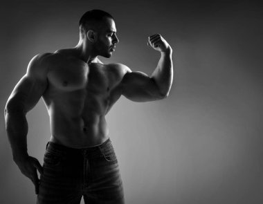 Çıplak vücutlu, güçlü, genç bir sporcu. Ayakta duruyor ve güçlü, şişkin pazılarını gösteriyor.