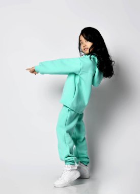 Modern yeşil, nane renginde kapüşonlu ve pantolonlu Asyalı kız parmak önde duruyor.