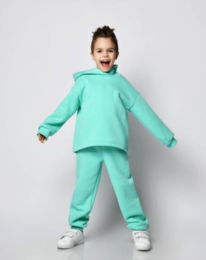 Mutlu çığlıklar atan, modern yeşil giysili, spor takım elbiseli çocuk ve pantolon el ele tutuşup duruyor.