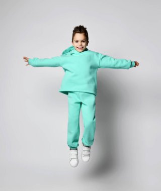 Neşeli, güler yüzlü, şık takım elbiseli yeşil, nane rengi kapüşonlu ve pantolonlu çocuk el ele tutuşarak zıplıyor.