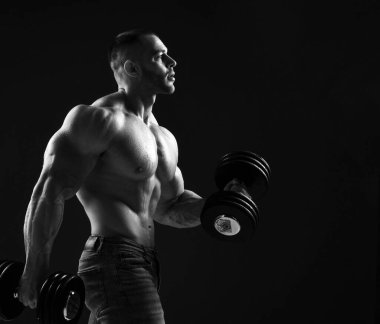 Güçlü, kaslı vücut geliştirme antrenörü iki dambıl kaldırıyor, pazılar için egzersiz yapıyor.