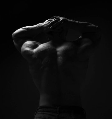 Kaslı bir adam, vücut geliştiren, ıslak atletik vücutlu, sırtında kameraya dönük, elleri başının arkasında duran tişörtsüz bir adam.