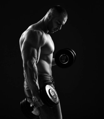 Kaslı adam vücut geliştirici, iki dambılı sırayla kaldırıyor, pazılar için egzersiz yapıyor.