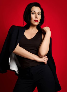 Güzel, kendine güvenen esmer kadın portresi şık bir iş elbisesi giymiş ayakta kameraya bakıyor.