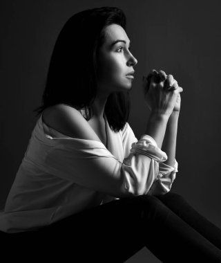 Gömleği ve pantolonu yerde oturan endişeli, esmer, güzel bir kadının siyah beyaz portresi. Yan görünüm