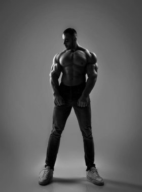 Yakışıklı kaslı erkeklerin siyah beyaz portresi. Vücut geliştirici. Elleri bacaklarında ve yana bakıyor.