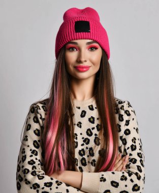 Pembe iplikli, parlak makyajlı, şık şapkalı, kameraya bakan genç ve varlıklı bir kadın.