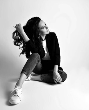 Gülümseyen olgun kadın portresi. Günlük iş kıyafetleri, kot pantolon ve ceket giyip saçlarına el ele otururken.