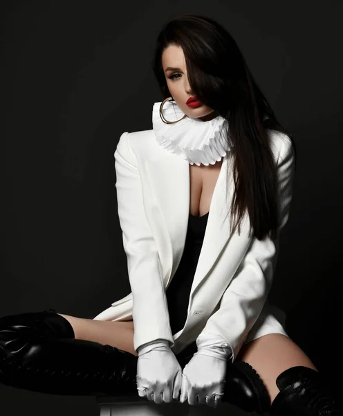 Sexig brunett söt kvinna modell i höga stövlar, jacka och krage sitter på pall tittar på kameran — Stockfoto