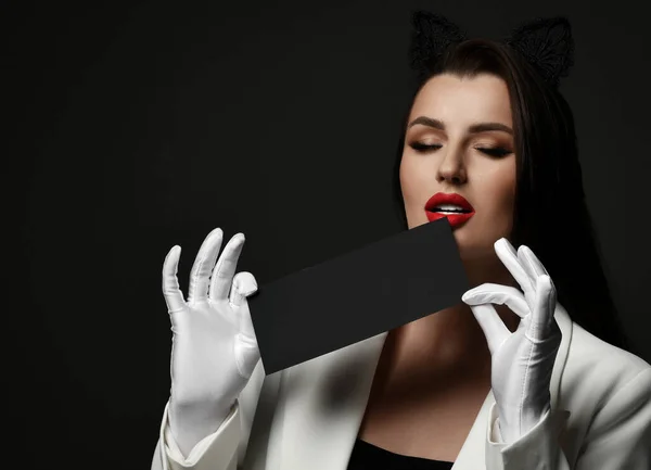 Sexy woman head waiter or steward in black cat ears band, white jacket and gloves holds black envelope at red lips — Stock Photo, Image