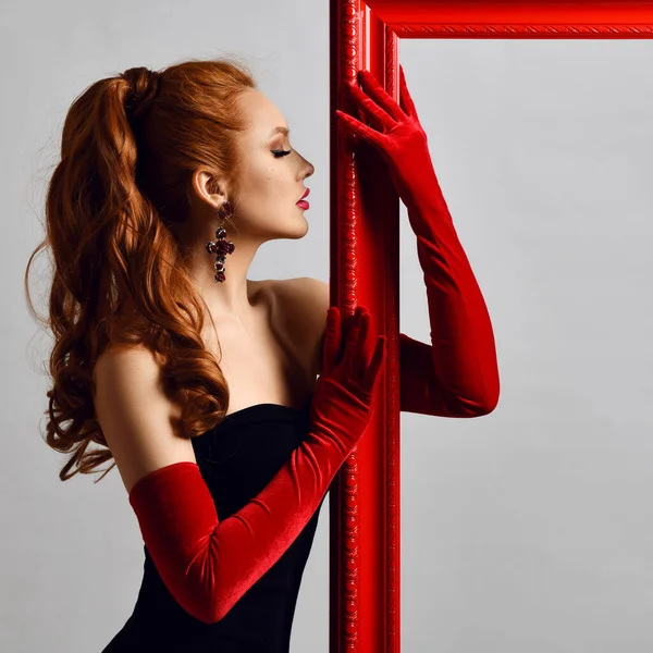 Opgewonden jonge vrouw artiest in zwart off-schouder strakke jurk, rode elleboog-lengte handschoenen sexy poseren op rode fotolijst — Stockfoto