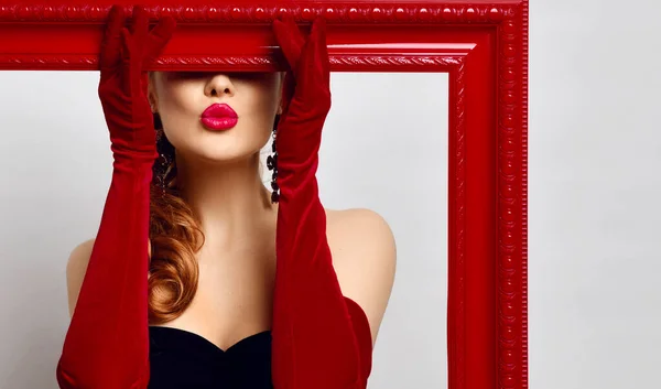 Young woman artist in black off-shoulder tight dress, red elbow-length gloves holds picture frame covering her eyes — Stock Photo, Image