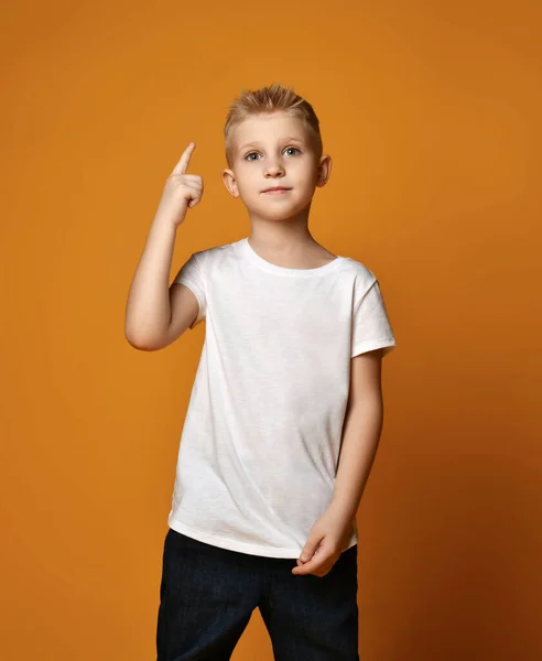 Niño de la escuela joven en camiseta blanca apuntando con el dedo índice hacia arriba o el dedo número uno mirando hacia arriba feliz. Fondo amarillo —  Fotos de Stock