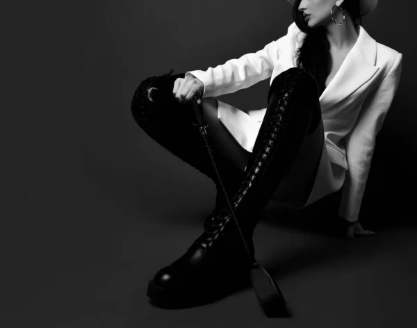 Business brunette pretty woman model in high boots and jacket sitting on floor holding whip in hand — Photo