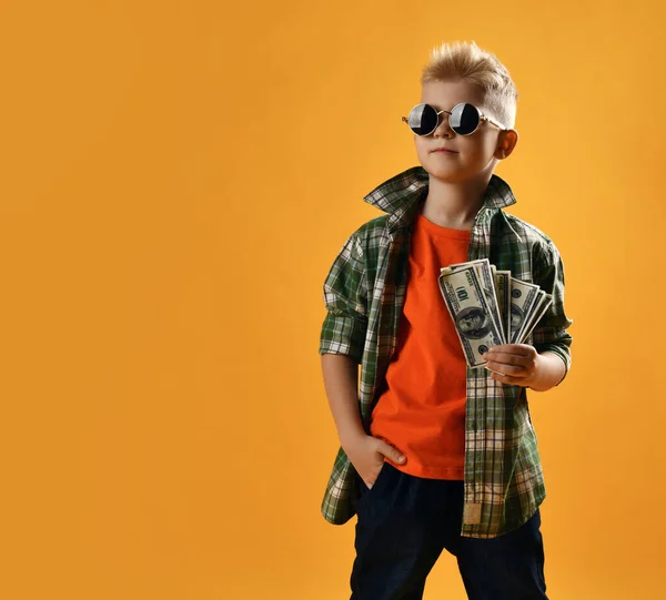 Ganador adolescente rico en calma en gafas de sol redondas, camisa a cuadros a cuadros y puestos de vaqueros sosteniendo ventilador de dólares en efectivo —  Fotos de Stock