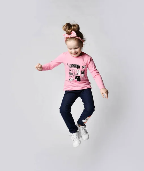 Веселая, весёлая девочка в синих порванных джинсах, розовая футболка с длинным рукавом и кроссовки прыгают высоко — стоковое фото