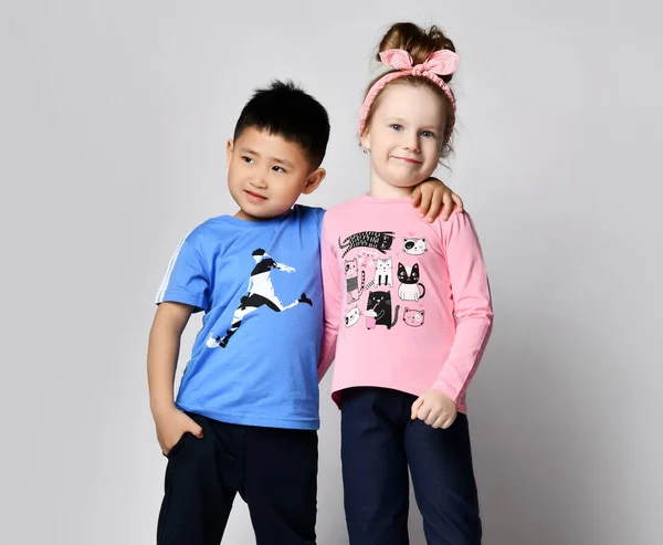 Little cute asian boy and blonde girl hold hands playing hugging on grey background. Happy family close up . brother and sister — Stock Photo, Image