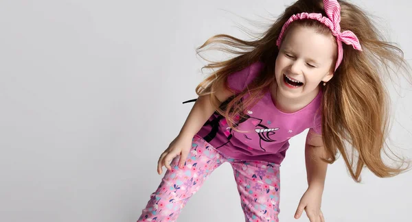 Cheerful kid girl in summer clothing colorful pants and t-shirt has fun jumping, dancing, shaking head, laughing loudly — Stock Photo, Image