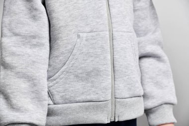 Gri kapüşonlu, fermuarlı, el ele tutuşup duran kız çocuğunun yakın çekimi.