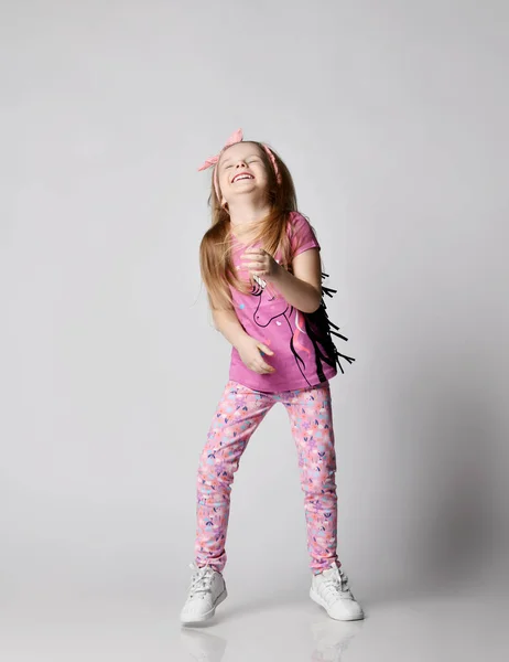 Κοριτσάκι με καλοκαιρινά ρούχα πολύχρωμο παντελόνι και t-shirt στέκεται με το κεφάλι πεταμένο πίσω και γελάει δυνατά — Φωτογραφία Αρχείου