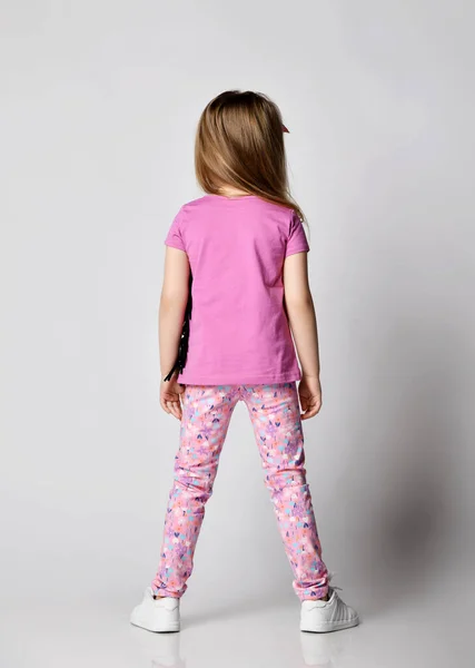 Маленькая блондинка девочка в летней одежде красочные брюки и розовая футболка стоит спиной к камере — стоковое фото