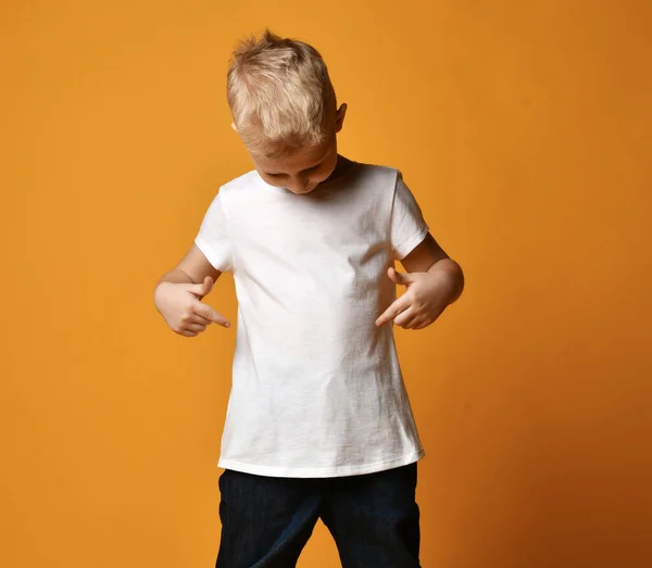 Niño rubio en camiseta blanca y jeans de pie y mirándose a sí mismo sobre fondo amarillo — Foto de Stock