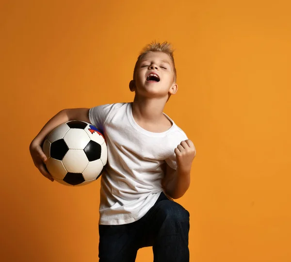 Menino feliz em branco t-shirt e jeans fica segurando bola de futebol na mão e celebra Objetivo — Fotografia de Stock