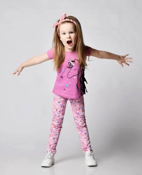 Frolic blonde kid girl in summer clothing colorful pants and t-shirt stands with her arms outstretched and screams — Stock Photo, Image