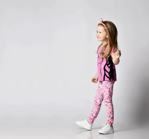 Happy frolic blonde kid girl in summer clothing colorful pants and t-shirt walks looking at copy space. Side view — Stock Photo, Image