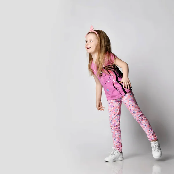 Playful curious blonde kid girl in summer clothing colorful pants and t-shirt stands peeking at copy space — Stock Photo, Image