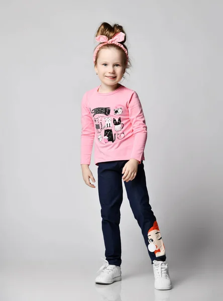 Active, having fun kid girl in pink long sleeve t-shirt and sneakers stands showing print on her blue jeans — Stock Photo, Image