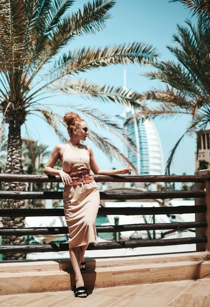 Rijk stijlvolle prachtige toeristische vrouw in de zomer jurk poseert op de achtergrond van beroemde Dubai wolkenkrabbers tijdens vakantie — Stockfoto