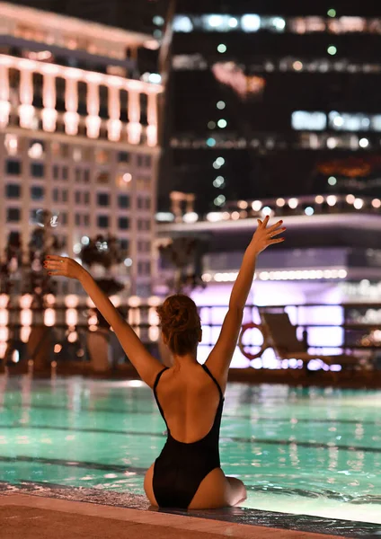 Happy sexy slanke vrouw poseert zitten aan de rand van het zwembad 's nachts tijdens vakantie in Dubai hand in hand — Stockfoto