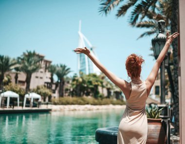 Yazlık elbiseli mutlu sarışın kadın. Dubai 'de tatilin tadını çıkarıyor. Birleşik Arap Emirlikleri' nde, elleri havada.