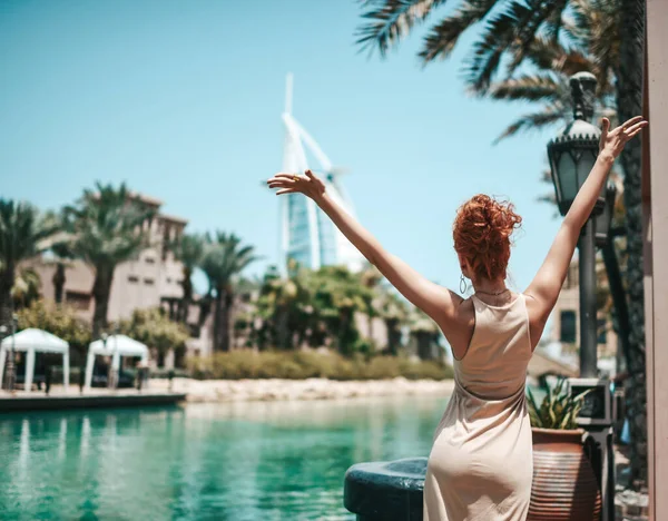 Yazlık elbiseli mutlu sarışın kadın. Dubai 'de tatilin tadını çıkarıyor. Birleşik Arap Emirlikleri' nde, elleri havada.