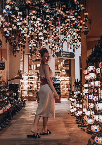 Радісна жінка з рудим волоссям в літньому вбранні насолоджується відвідуванням вуличного ринку в Дубаї, відвідуючи магазин ліхтарів. — стокове фото