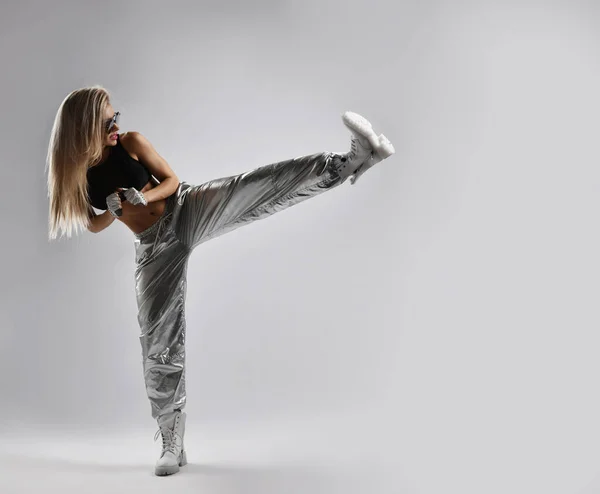 运动的，运动的女人，穿着宽松的银色裤子的拳击手，黑色的运动上衣，粗野的鞋子踢，抬起腿 — 图库照片