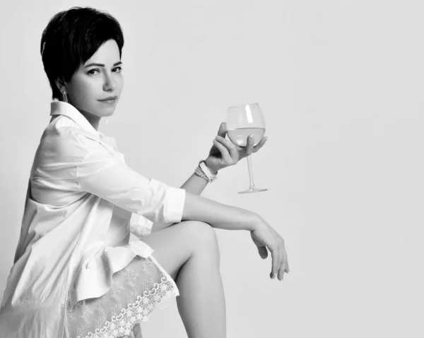 Чорно-білий портрет брюнетки в білому мереживній сукні і куртці, що тримає келих білого вина над світлом — стокове фото