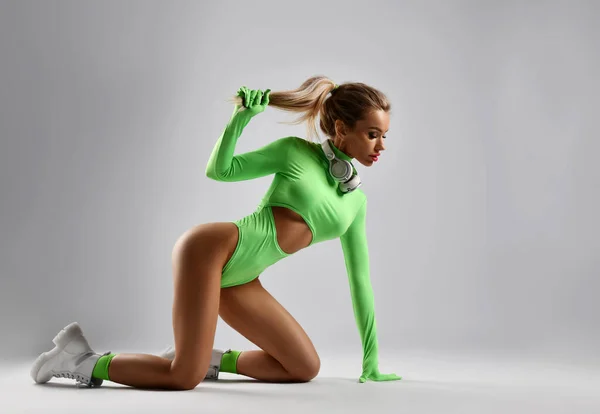 Sexy excited slim sporty blonde woman in stylish sportswear bodysuit stands on all fours holding her hair in hand —  Fotos de Stock