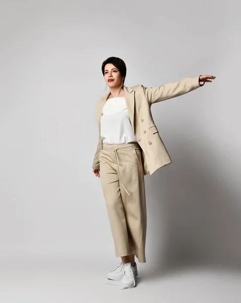 Adult pretty brunette woman walks in beige business smart casual pantsuit and sneakers. Stylish business female wear — Stock Photo, Image