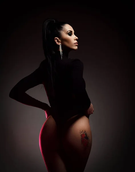 Silhouette of Beautiful young brunette woman in black string body standing showing tattoo on perfect buttocks —  Fotos de Stock