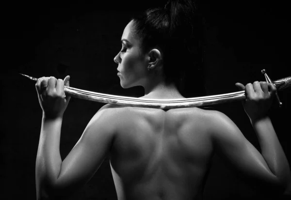 Svart och vitt porträtt av ung söt brunett topless kvinna poserar tillbaka till kameran håller svärd på axlarna — Stockfoto