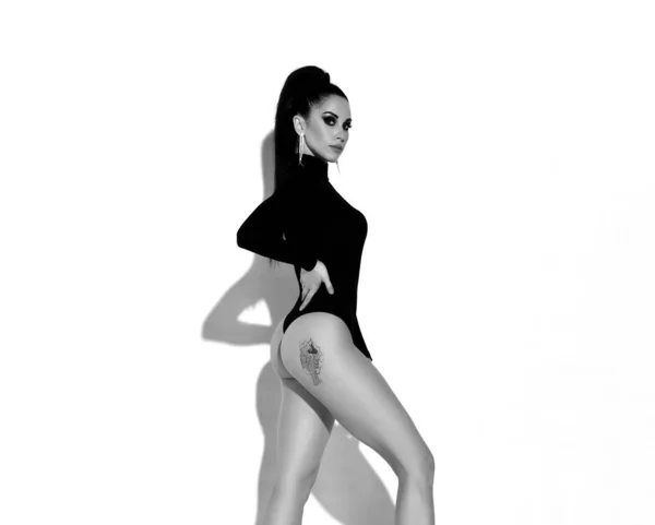 Potret hitam dan putih dari wanita berambut cokelat seksi langsing dalam tubuh benang hitam berdiri menyamping menunjukkan tato di bokong — Stok Foto