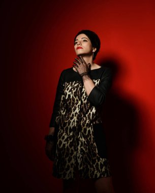 Düşünceli romantik kısa saçlı esmer kadın leopar desenli elbise ve dantel eldivenler yukarı bakıyor.