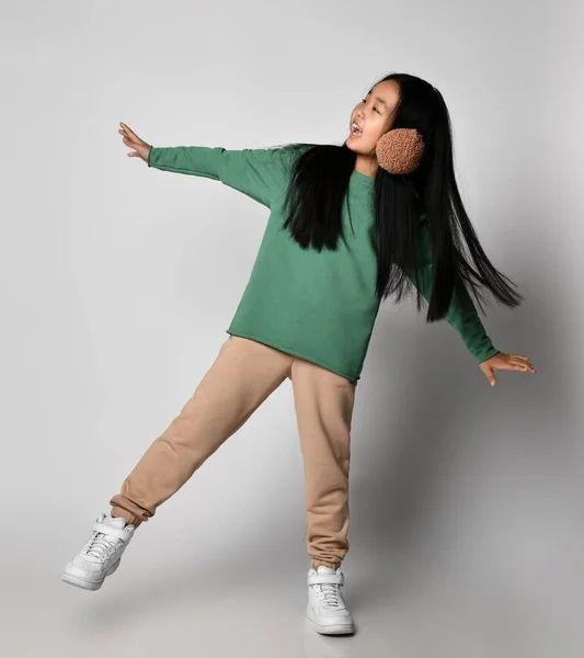 Yeşil spor giyim ve beyaz spor ayakkabılı Asyalı kız kollarını açmış, dengede duruyor. — Stok fotoğraf