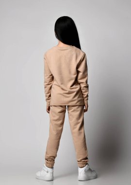 Tanımlanamayan esmer, yeşil pantolonlu, kapüşonlu, kazaklı ve spor ayakkabılı genç kız kameraya arkasını döner.