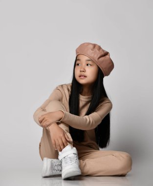 Asyalı esmer kız yeşil bereli, pantolonlu, kapüşonlu, kazaklı ve spor ayakkabılı.