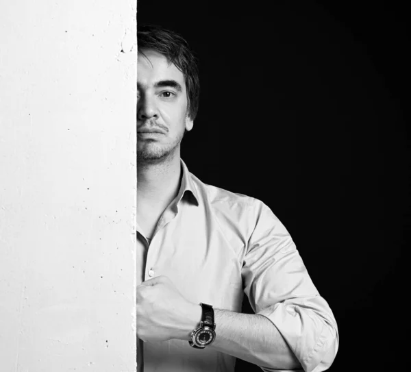 Черно-белый портрет мужчины средних лет в рубашке, стоящего за белой бетонной стеной и ударяющего кулаком о стену — стоковое фото